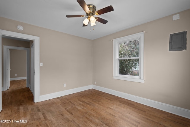 spare room with ceiling fan, wood finished floors, electric panel, and baseboards