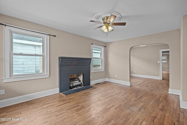 unfurnished living room featuring a ceiling fan, arched walkways, baseboards, and wood finished floors