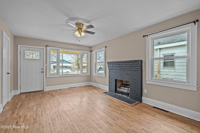 unfurnished living room featuring baseboards, a brick fireplace, visible vents, and light wood-style floors