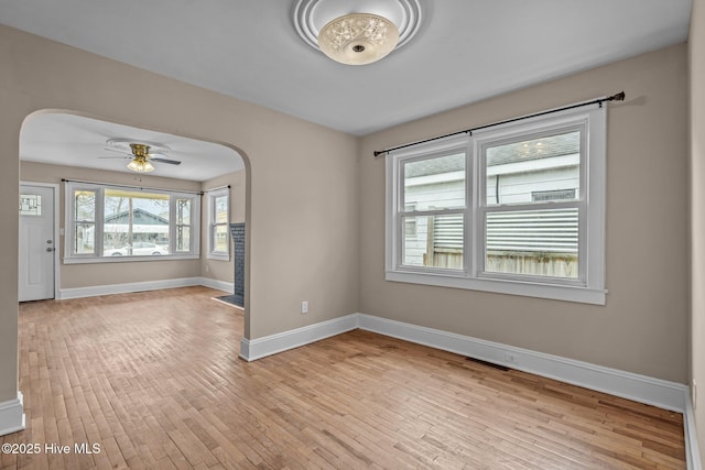 empty room with light wood-style floors, baseboards, arched walkways, and a ceiling fan