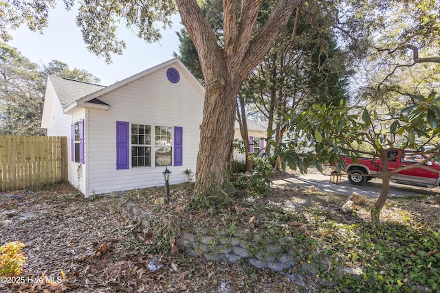 view of home's exterior featuring a shingled roof and fence