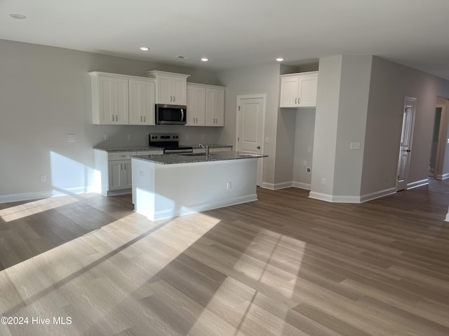 kitchen with recessed lighting, wood finished floors, white cabinets, appliances with stainless steel finishes, and a center island with sink