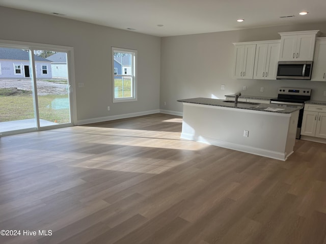 kitchen featuring light wood finished floors, stainless steel appliances, a wealth of natural light, a sink, and dark stone countertops