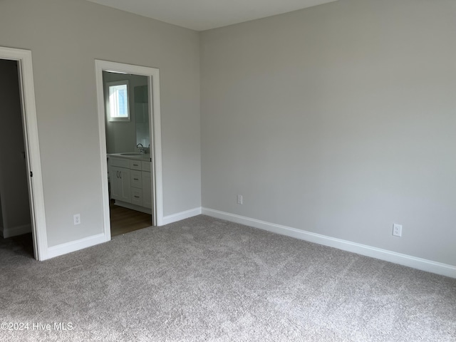 unfurnished bedroom with dark carpet, a sink, ensuite bath, and baseboards