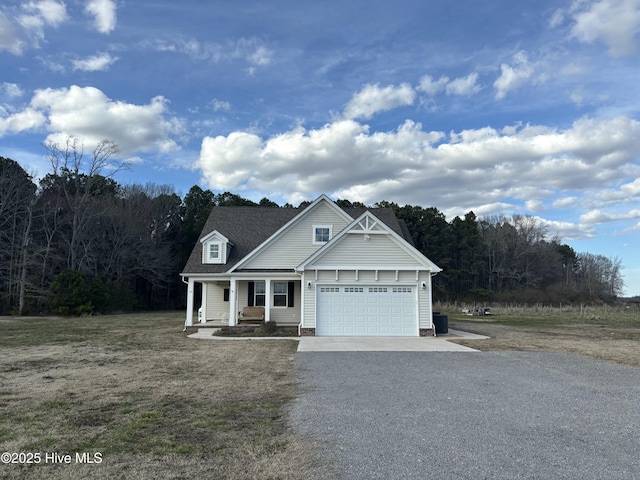 view of front of property featuring gravel driveway, covered porch, a garage, and a front yard