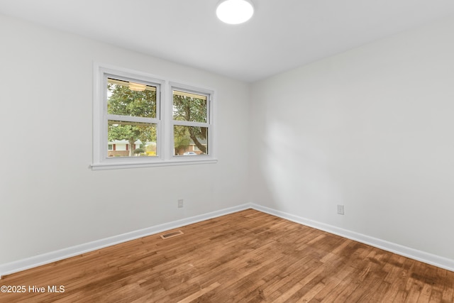 unfurnished room featuring wood finished floors, visible vents, and baseboards