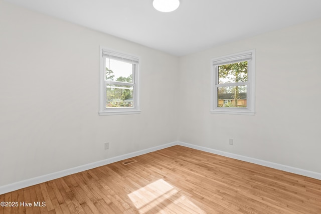 unfurnished room with light wood finished floors, a wealth of natural light, visible vents, and baseboards