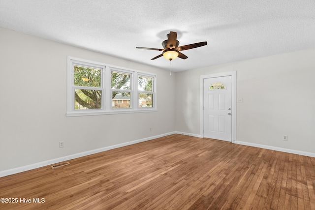 spare room with wood-type flooring, a textured ceiling, visible vents, and baseboards