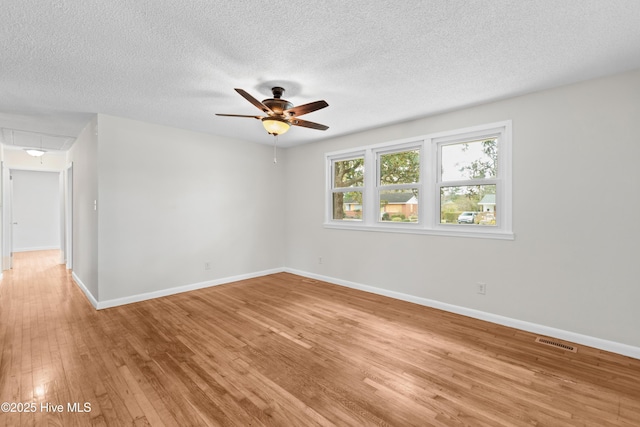 unfurnished room with light wood finished floors, attic access, baseboards, and ceiling fan