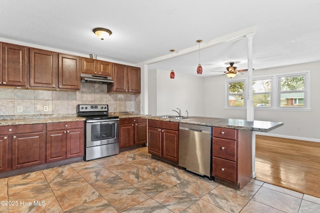 kitchen featuring under cabinet range hood, a sink, appliances with stainless steel finishes, tasteful backsplash, and decorative light fixtures