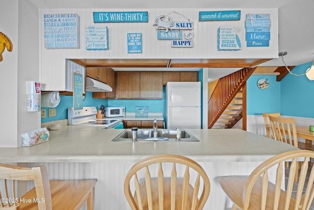 kitchen featuring white appliances, a kitchen breakfast bar, a peninsula, under cabinet range hood, and a sink