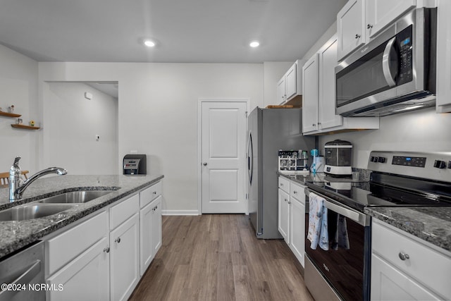 kitchen featuring dark stone counters, appliances with stainless steel finishes, a sink, and white cabinets