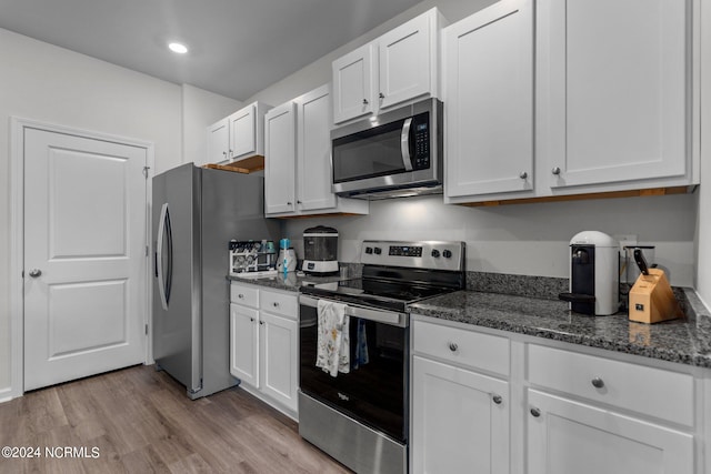 kitchen with dark stone countertops, stainless steel appliances, light wood-type flooring, and white cabinetry