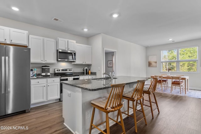 kitchen featuring dark wood-style floors, stainless steel appliances, a kitchen island with sink, a sink, and a kitchen bar