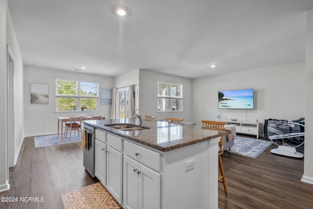 kitchen featuring a sink, white cabinetry, stainless steel dishwasher, dark stone counters, and an island with sink