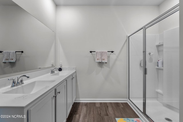 bathroom featuring double vanity, wood finished floors, a stall shower, and a sink