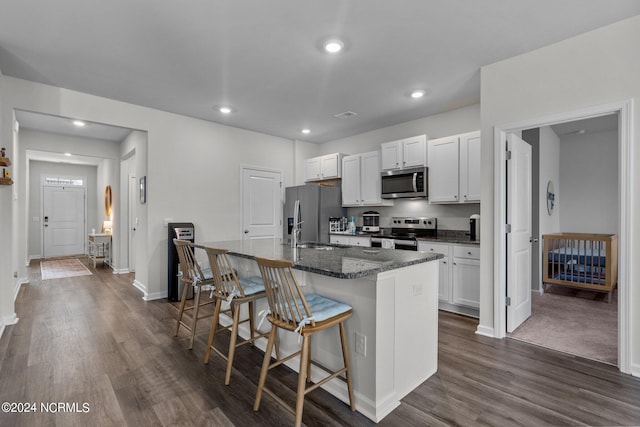 kitchen featuring recessed lighting, a breakfast bar, appliances with stainless steel finishes, dark wood-style floors, and a center island with sink