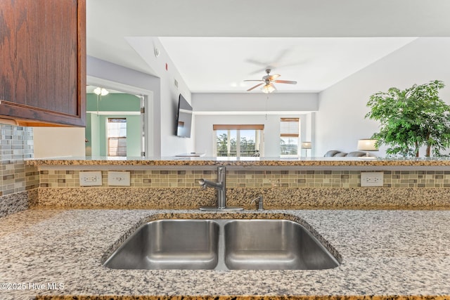 kitchen featuring a ceiling fan, tasteful backsplash, light stone counters, and a sink