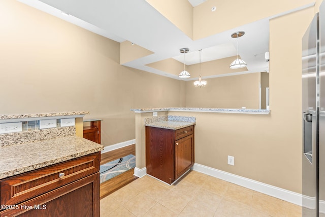 kitchen with a peninsula, baseboards, light stone countertops, an inviting chandelier, and pendant lighting