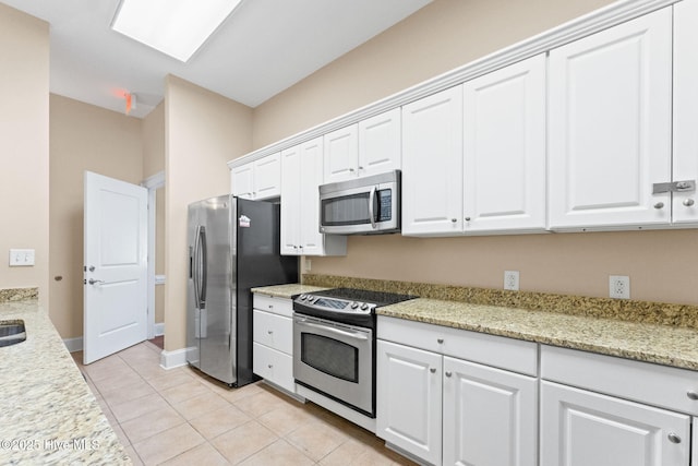 kitchen with appliances with stainless steel finishes, light tile patterned flooring, light stone countertops, and white cabinets