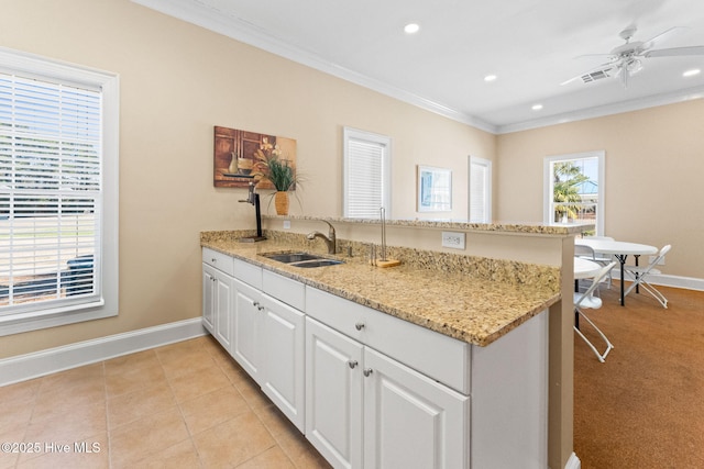 kitchen featuring baseboards, white cabinets, a peninsula, crown molding, and a sink