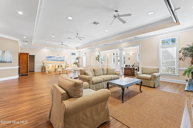 living area with light wood-style flooring, visible vents, a raised ceiling, and crown molding