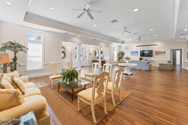 living room with light wood finished floors, a raised ceiling, visible vents, ornamental molding, and ornate columns