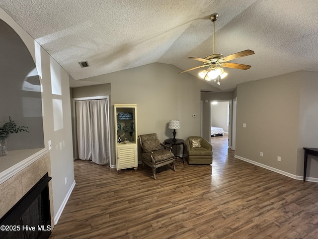 living area featuring a tile fireplace, dark wood-type flooring, a ceiling fan, baseboards, and vaulted ceiling