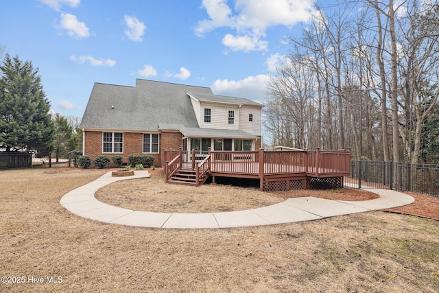 back of house featuring a shingled roof, a lawn, fence, a deck, and brick siding