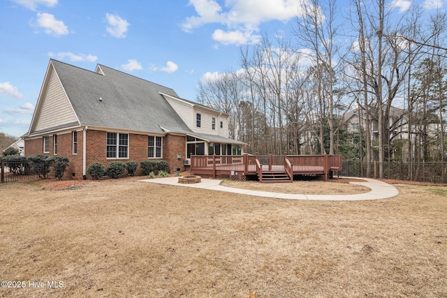 rear view of house with a deck, an outdoor fire pit, a shingled roof, brick siding, and fence