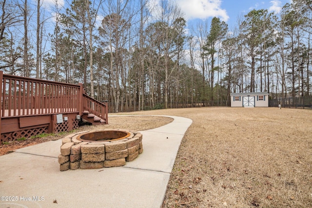 view of yard featuring a storage shed, a fire pit, an outbuilding, fence, and a deck