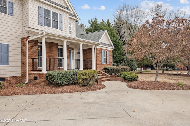 exterior space featuring a porch, crawl space, a shingled roof, and brick siding