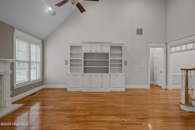 unfurnished living room featuring light wood finished floors, baseboards, visible vents, and high vaulted ceiling