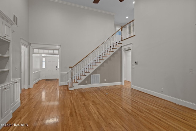 foyer entrance with light wood finished floors, visible vents, ornamental molding, baseboards, and stairs