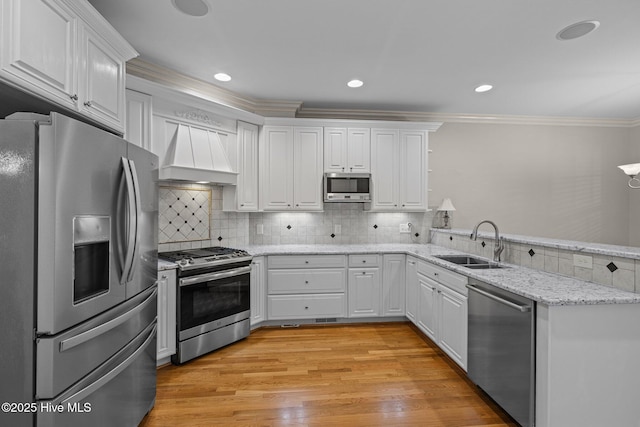 kitchen with stainless steel appliances, premium range hood, a sink, white cabinetry, and crown molding