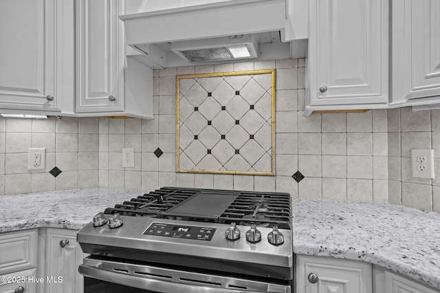 kitchen featuring light stone counters, stainless steel range with gas stovetop, extractor fan, white cabinetry, and backsplash