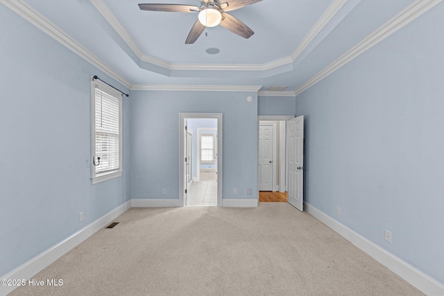 carpeted empty room with a raised ceiling, visible vents, ornamental molding, ceiling fan, and baseboards