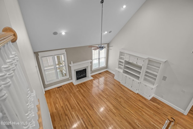 unfurnished living room featuring light wood finished floors, a premium fireplace, baseboards, and a ceiling fan