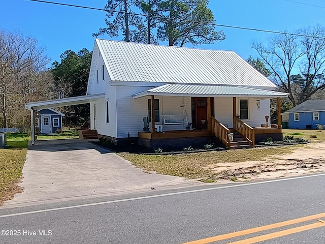 view of front of home with an outbuilding, covered porch, metal roof, an attached carport, and driveway