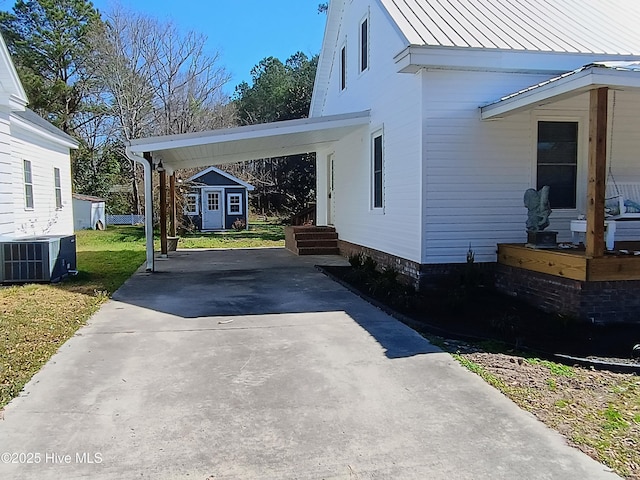 view of side of property with concrete driveway, a lawn, central AC unit, a standing seam roof, and metal roof