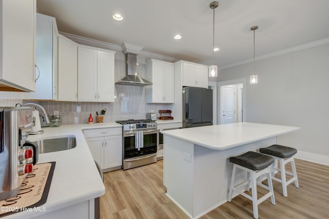 kitchen with tasteful backsplash, freestanding refrigerator, stainless steel range with gas stovetop, a sink, and wall chimney range hood