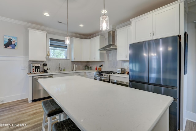 kitchen with a sink, ornamental molding, appliances with stainless steel finishes, decorative backsplash, and wall chimney exhaust hood