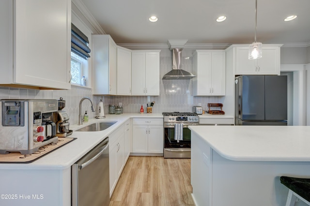 kitchen with stainless steel appliances, a sink, light countertops, ornamental molding, and wall chimney range hood