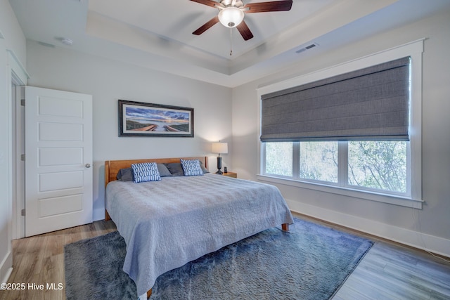 bedroom featuring baseboards, visible vents, a tray ceiling, and wood finished floors