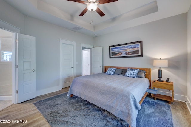 bedroom featuring ceiling fan, light wood-style flooring, visible vents, baseboards, and a tray ceiling