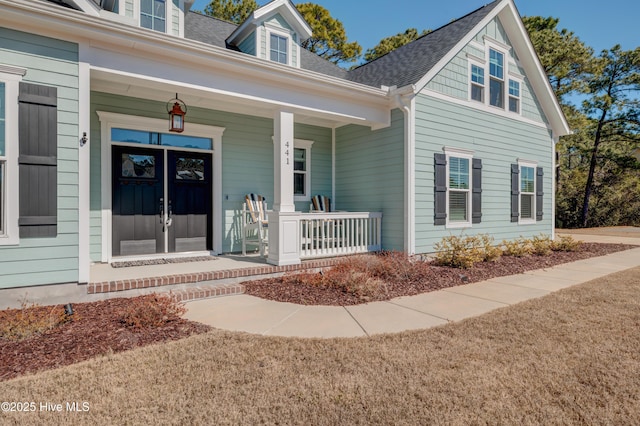 view of exterior entry with a shingled roof and covered porch