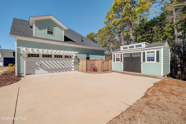 view of front of property featuring a garage, a shingled roof, concrete driveway, an outbuilding, and fence