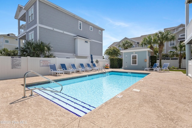 community pool with a patio area, fence, and an outdoor structure