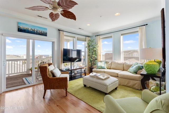 living room featuring light wood finished floors, visible vents, and crown molding