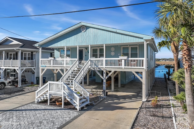 beach home featuring covered porch, concrete driveway, a carport, and stairway